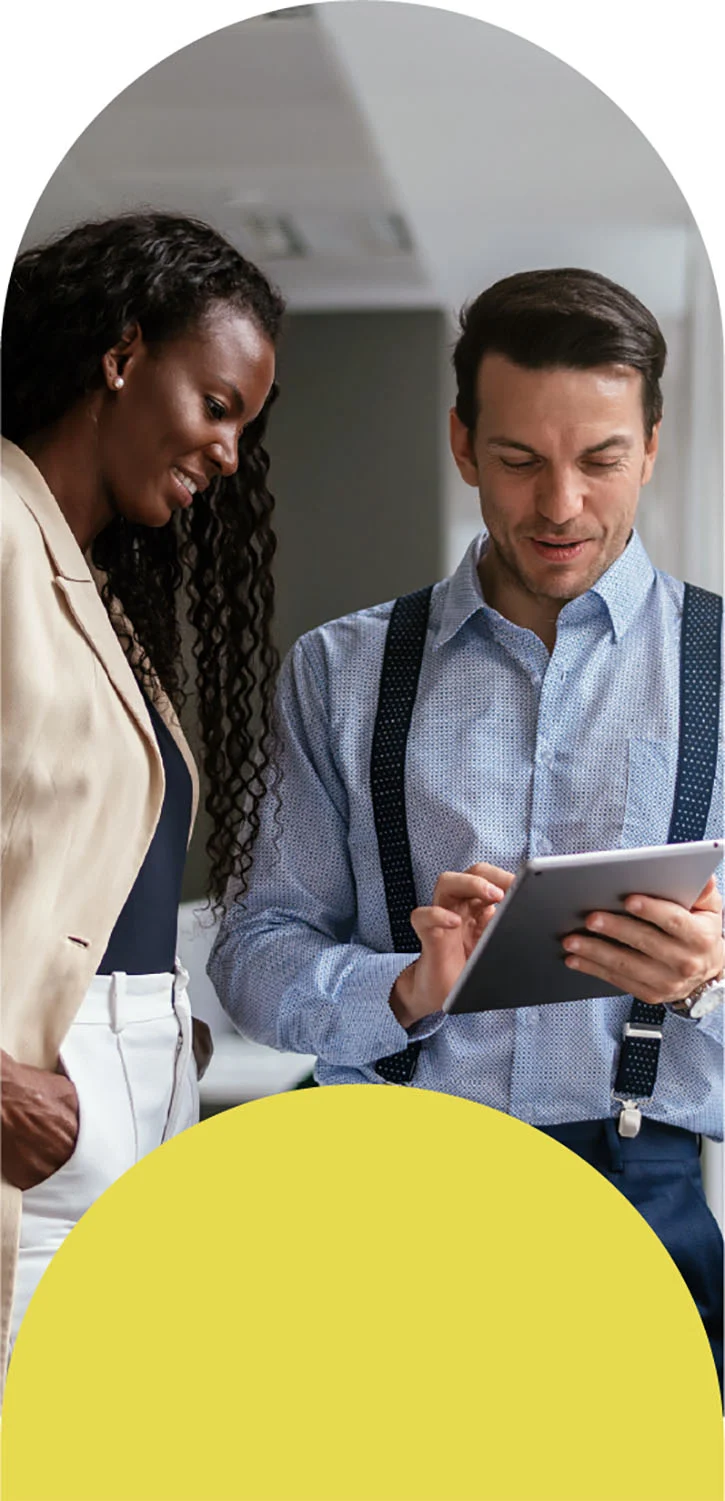 Two people discussing something while one holds a tablet and the other has hands in pockets.