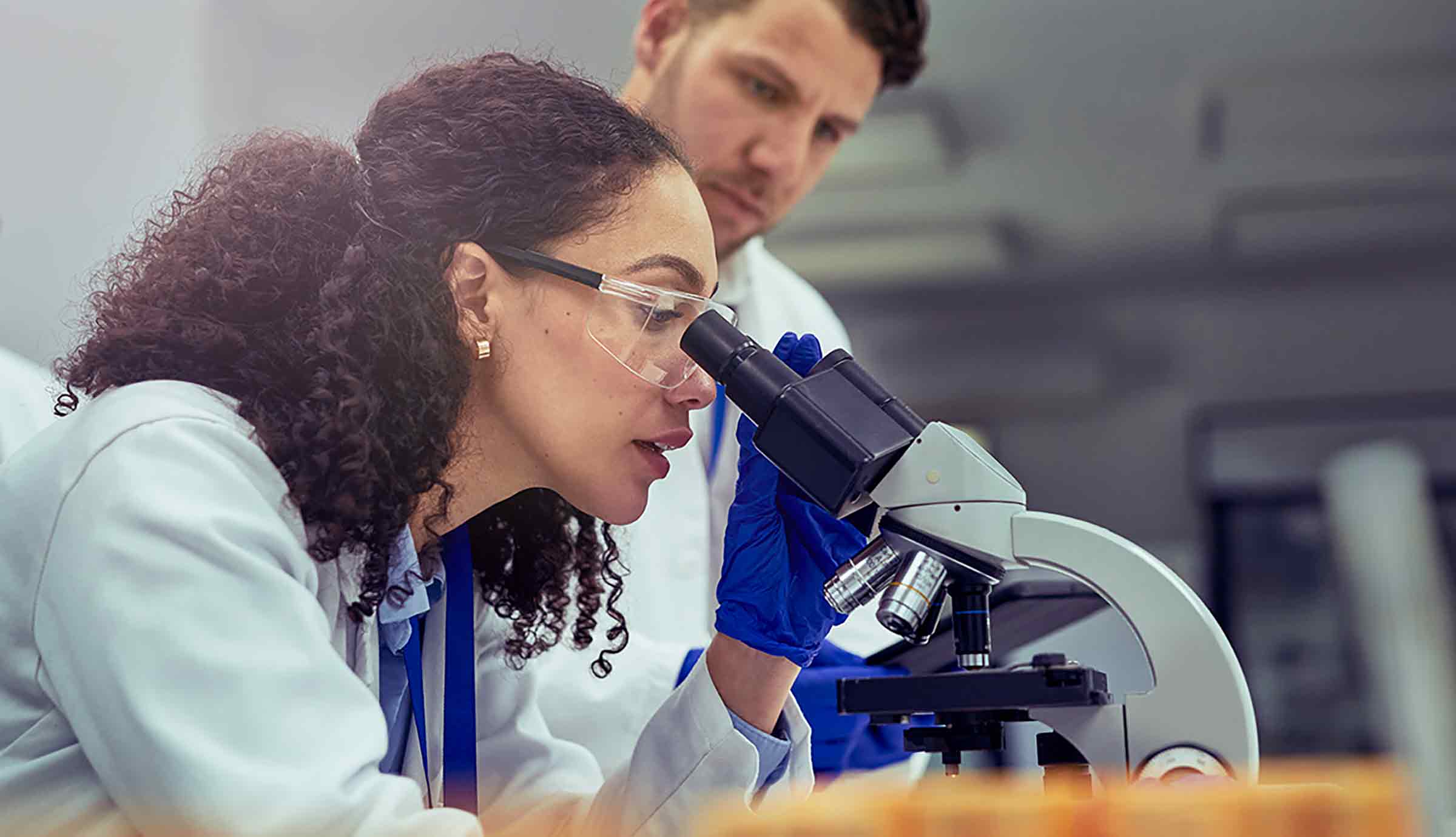 researchers in lab coats looking into a microscope.