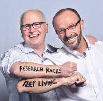 Two people, one in stripes and one in white, showing forearms with "RESEARCH ROCKS" and "KEEP LIVING" written on them.